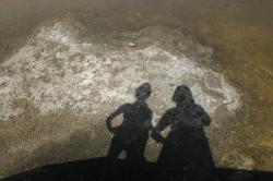 Two people cast shadows onto shallow water at the Alviso salt marshes.